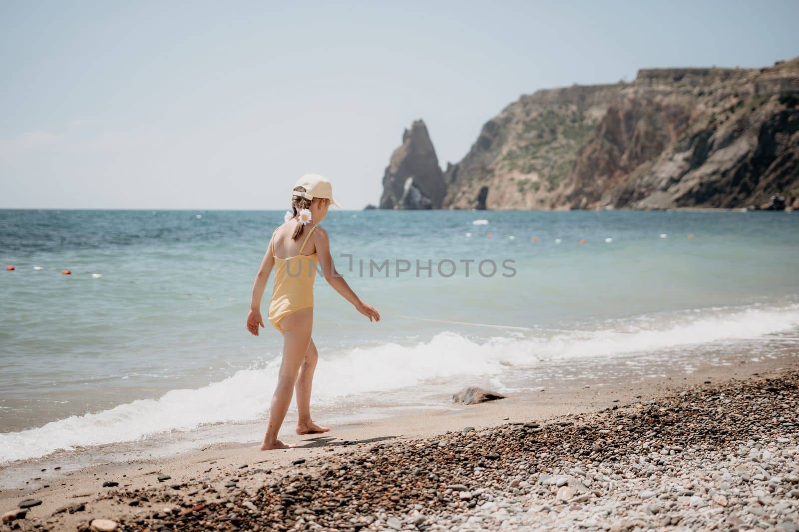 Cute little girl running along the seashore against a clear blue sea and rejoices in the rays of the summer sun. Beautiful girl in yellow swimsuit running and having fun on tropical beach. by panophotograph