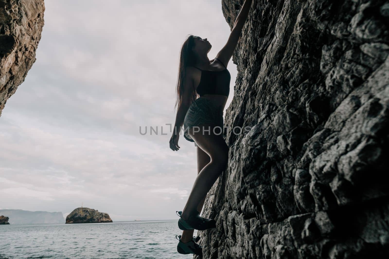 A girl climbs a rock. The athlete trains in nature. Woman overcomes difficult climbing route. Extreme hobby. Tourist woman rock climber hiking on mountains rocks over beautiful sea coast