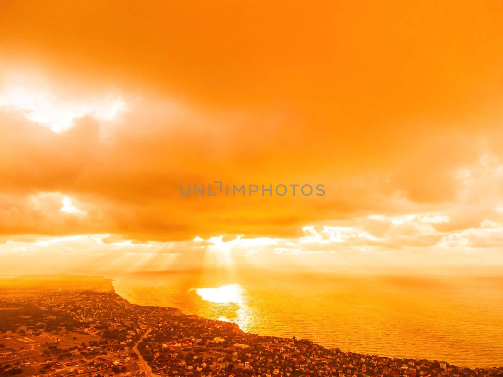A red burning sunset with the silhouette of a cliff over the sea. Abstract nature summer or spring ocean sea background. Small waves on golden warm water surface with bokeh lights from sun.