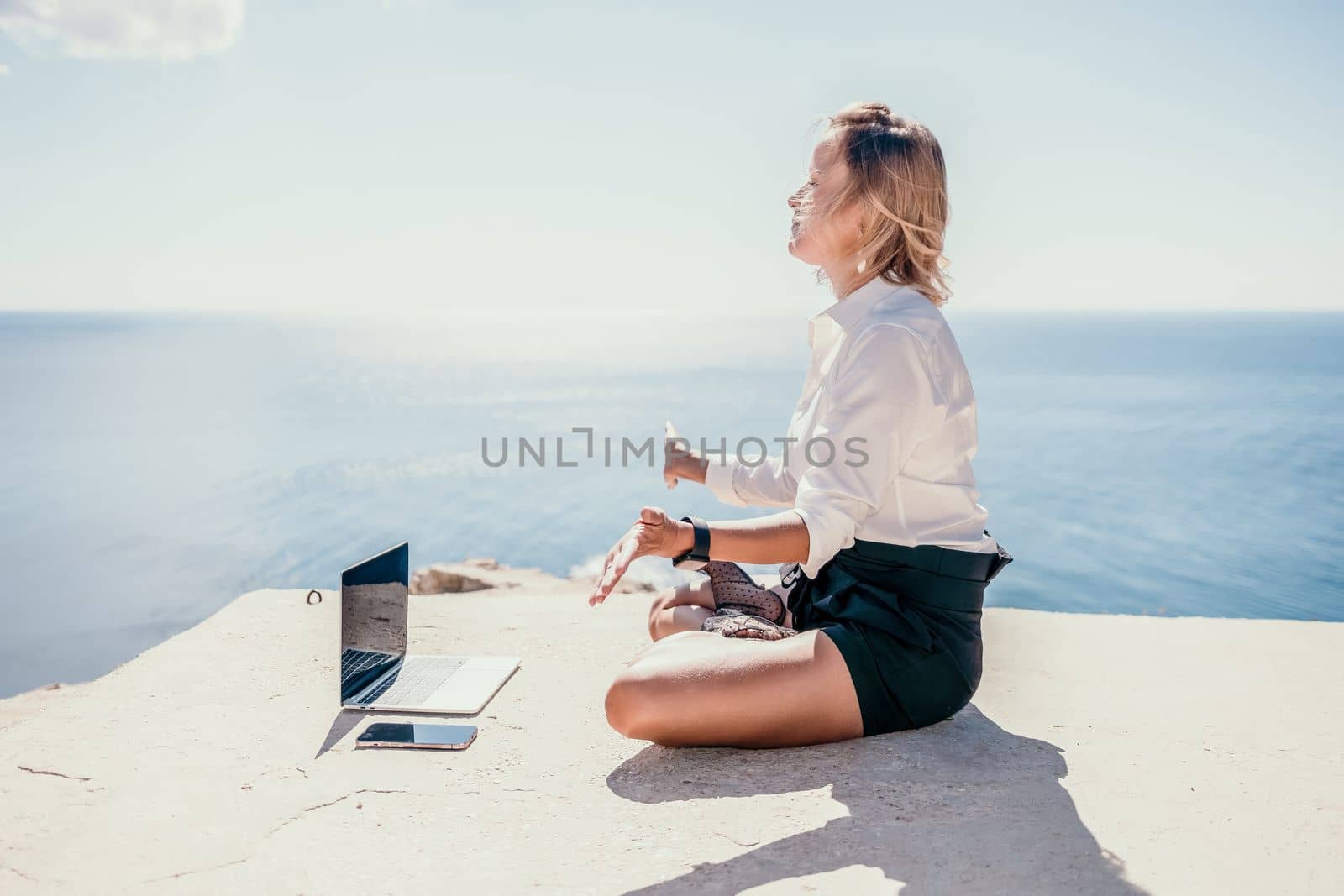 Happy girl doing yoga with laptop working at the beach. beautiful and calm business woman sitting with a laptop in a summer cafe in the lotus position meditating and relaxing. freelance girl remote work beach paradise