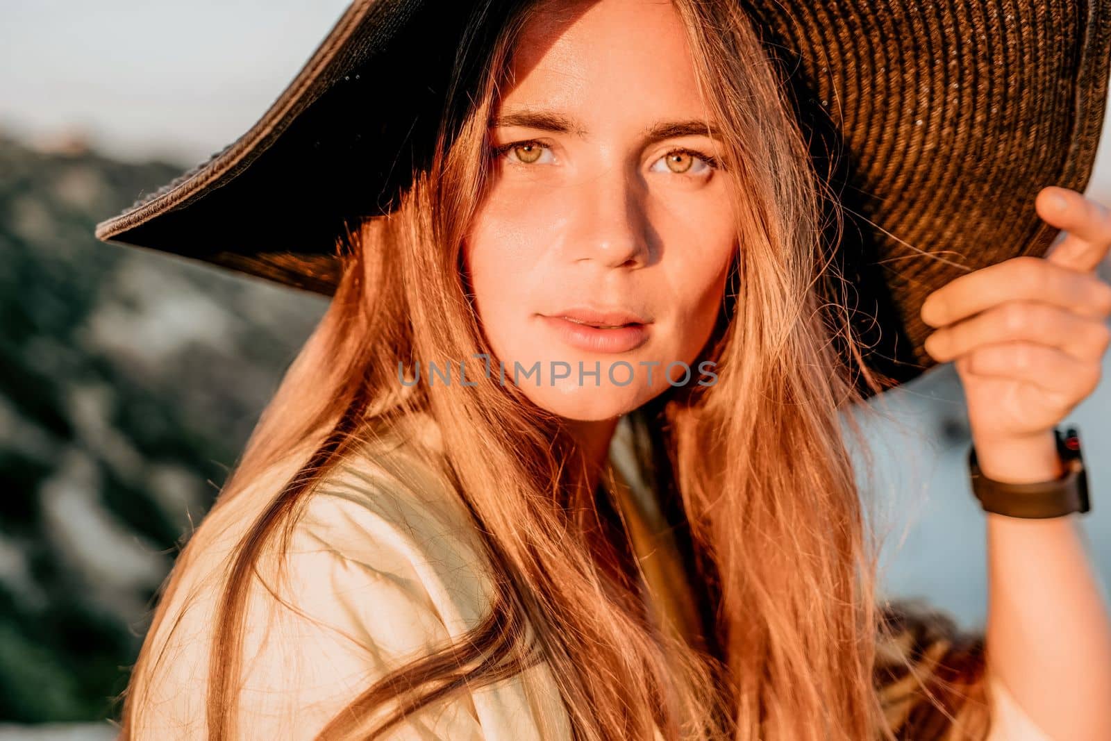 Portrait of happy young woman wearing summer black hat with large brim at beach on sunset. Closeup face of attractive girl with black straw hat. Happy young woman smiling and looking at camera at sea