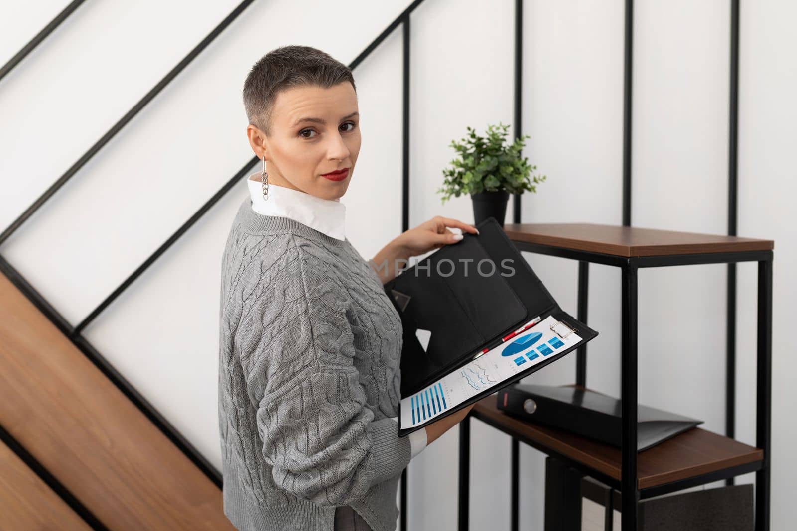 A business woman with a short haircut stands in the office with a folder for documents..