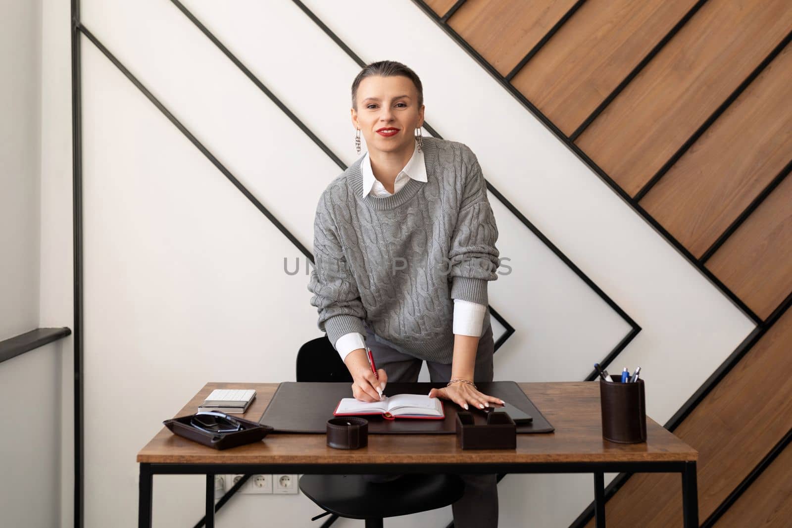 Businesswoman with short haircut in gray sweater at desk in office.