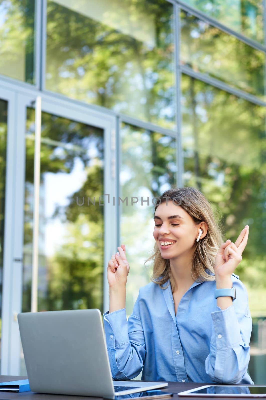 Portrait of smiling and excited businesswoman sitting with laptop, makes crossed fingers gesture, makes wish, praying, working outdoors.
