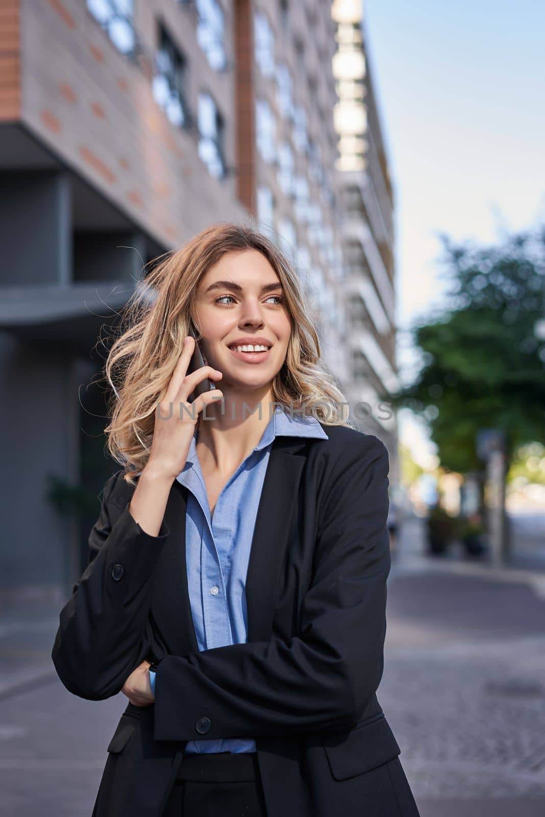 Vertical shot of confident young businesswoman making phone call, standing on street and talking on telephone.