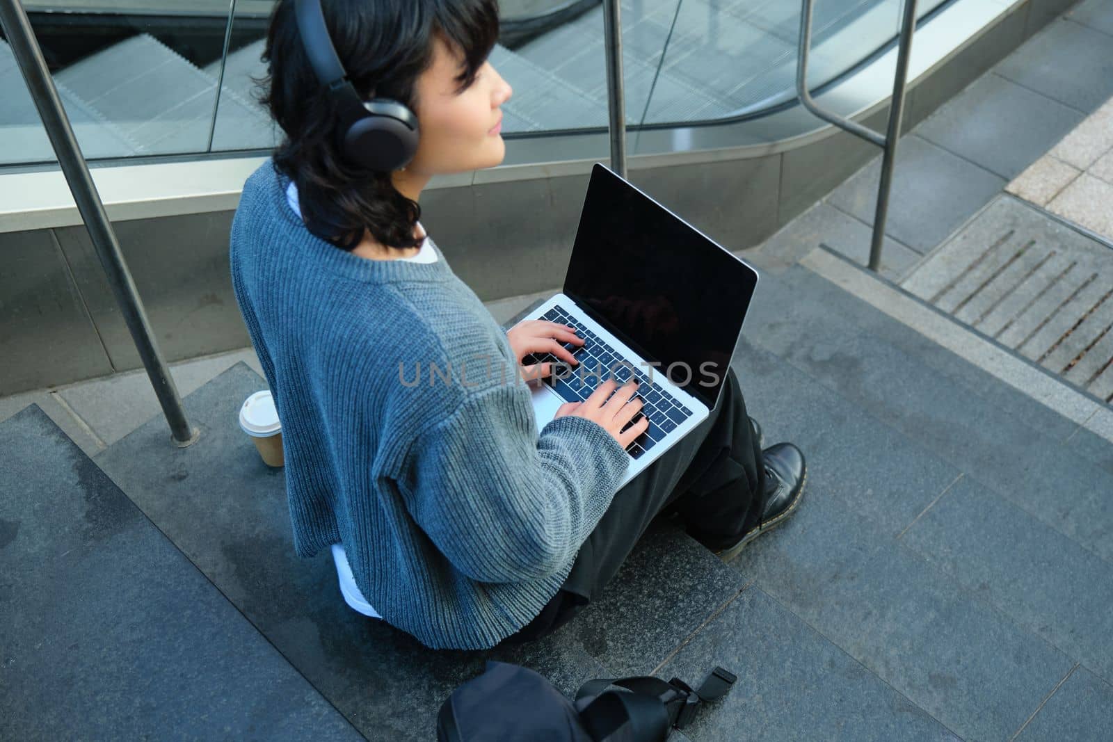 Close up portrait of girl, student works on laptop and listens music in headphones. Blank computer screen and hands typing on keyboard.