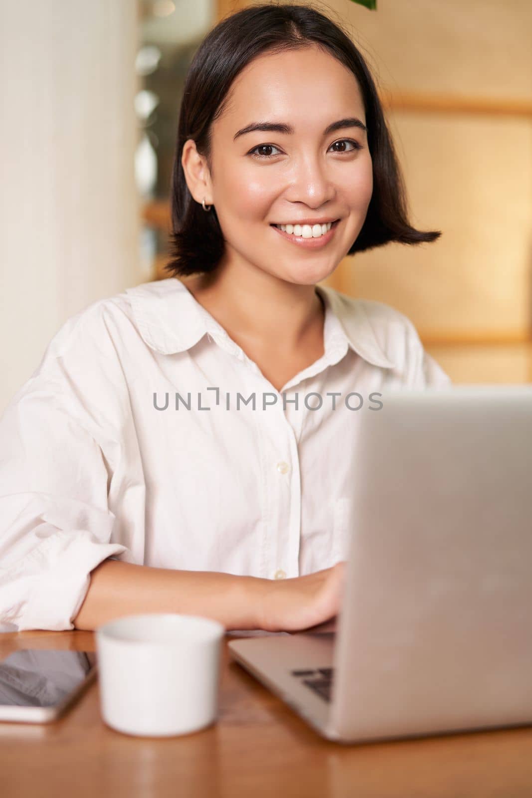 Stylish brunette woman with laptop, sitting in cafe and drinking coffee, smiling happily. People and lifestyle concept