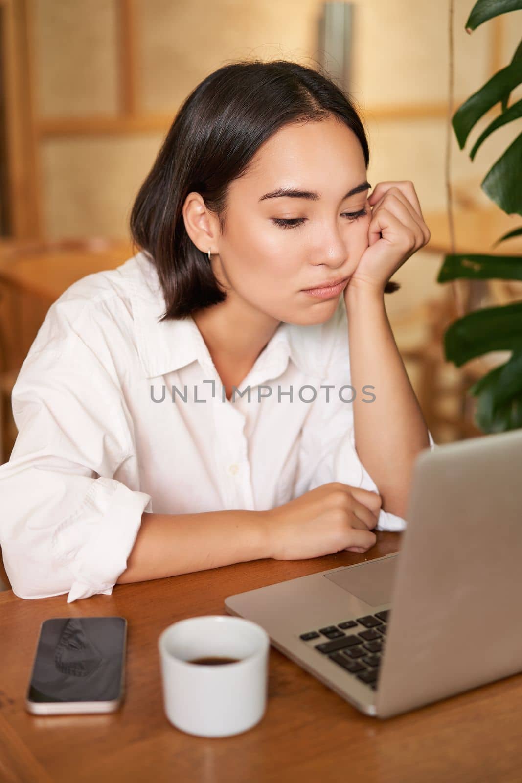 Vertical shot of asian girl looking tired at laptop screen, bored of working, sitting in cafe sleepy and exhausted by Benzoix