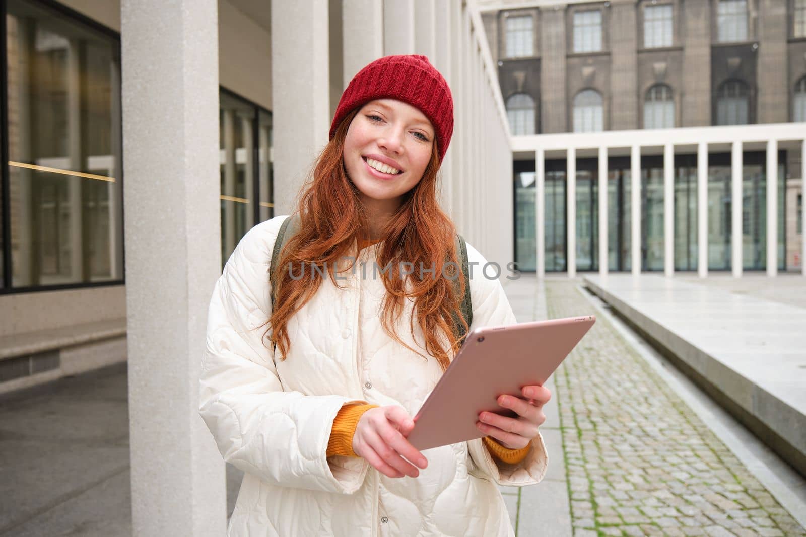 Stylish ginger girl, tourist walks with digital tablet around city, woman connects to iternet on her gadget, looking up information, texting message by Benzoix