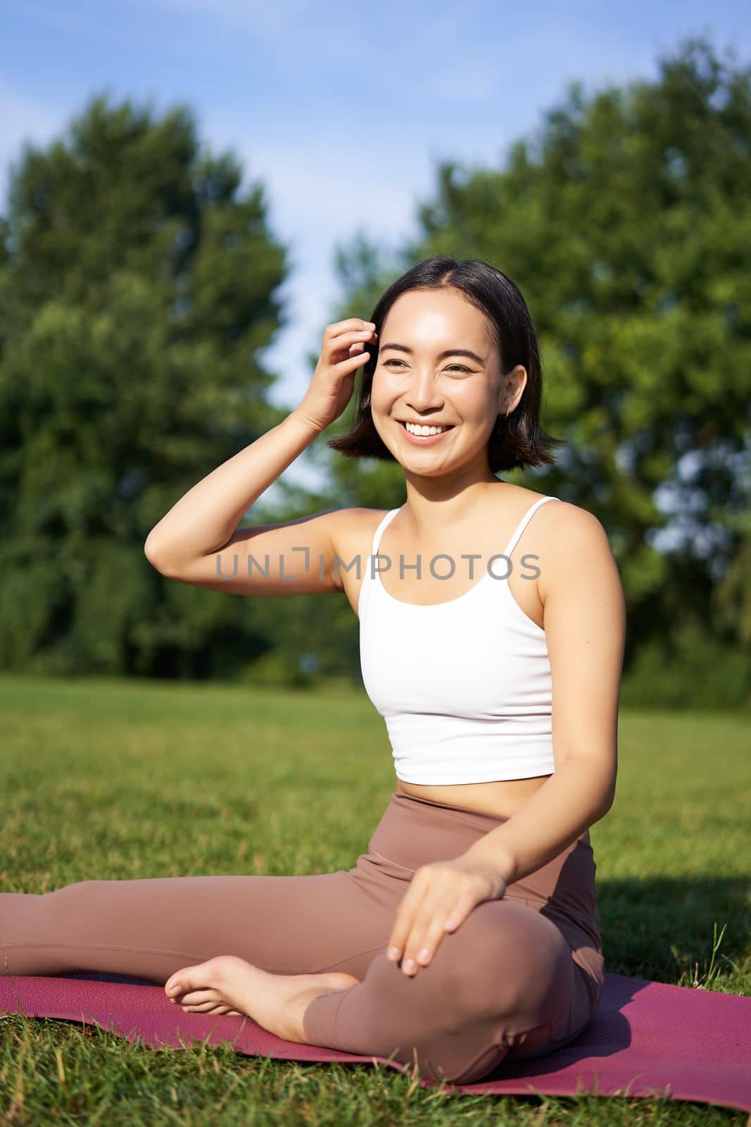 Meditation and mindfulness. Young asian woman smiling on fitness mat in park, doing yoga training, meditating on fresh air.