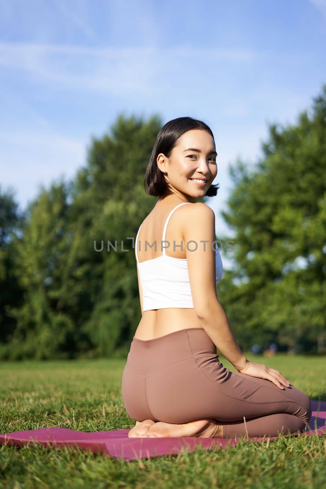 Portrait of asian woman sitting and meditating in park, doing yoga on fresh air, fitness exercises, smiling at camera by Benzoix