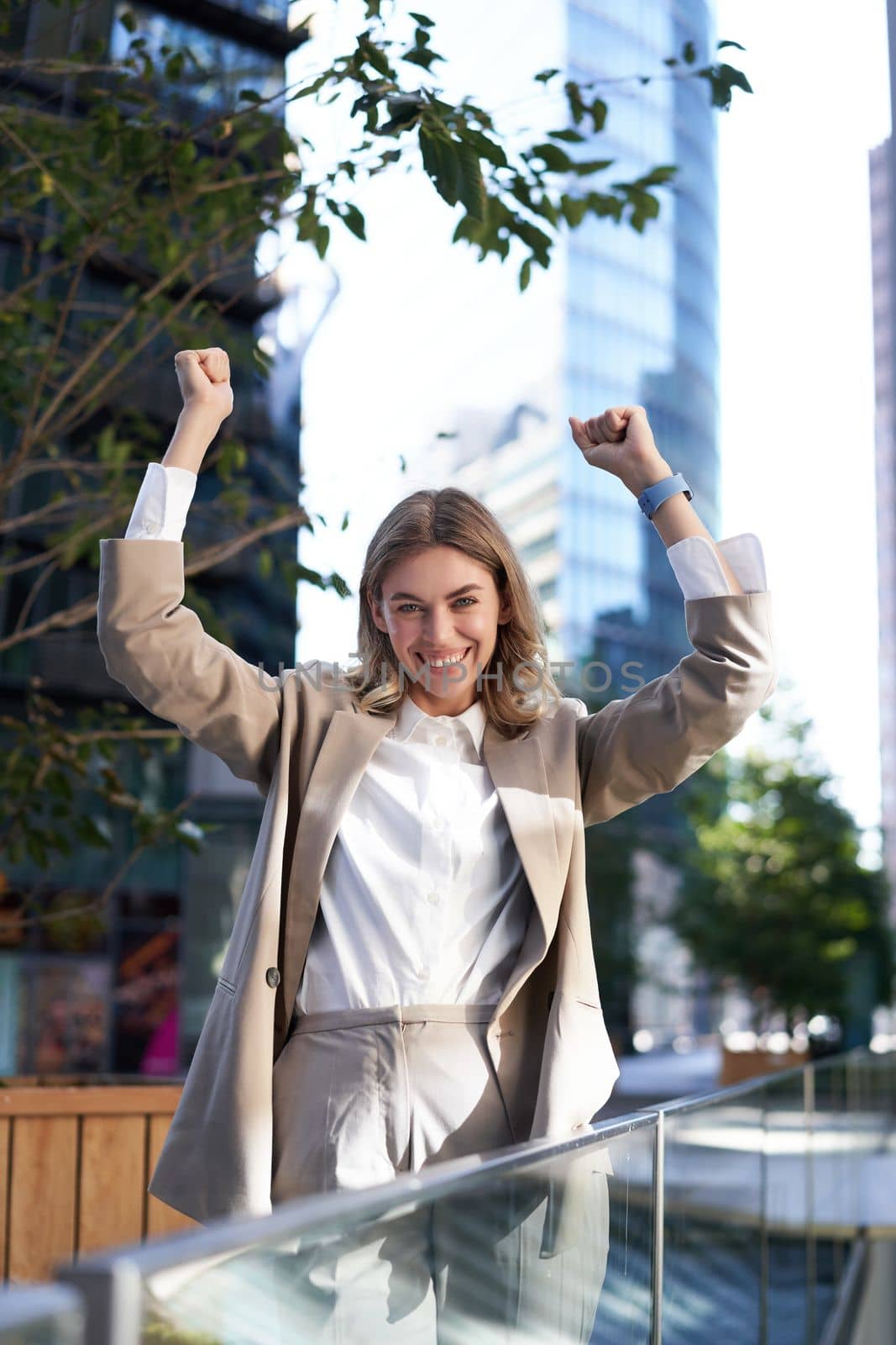Saleswoman expresses joy and happiness. Businesswoman triumphing on street, raising hands up, celebrating victory, smiling pleased.