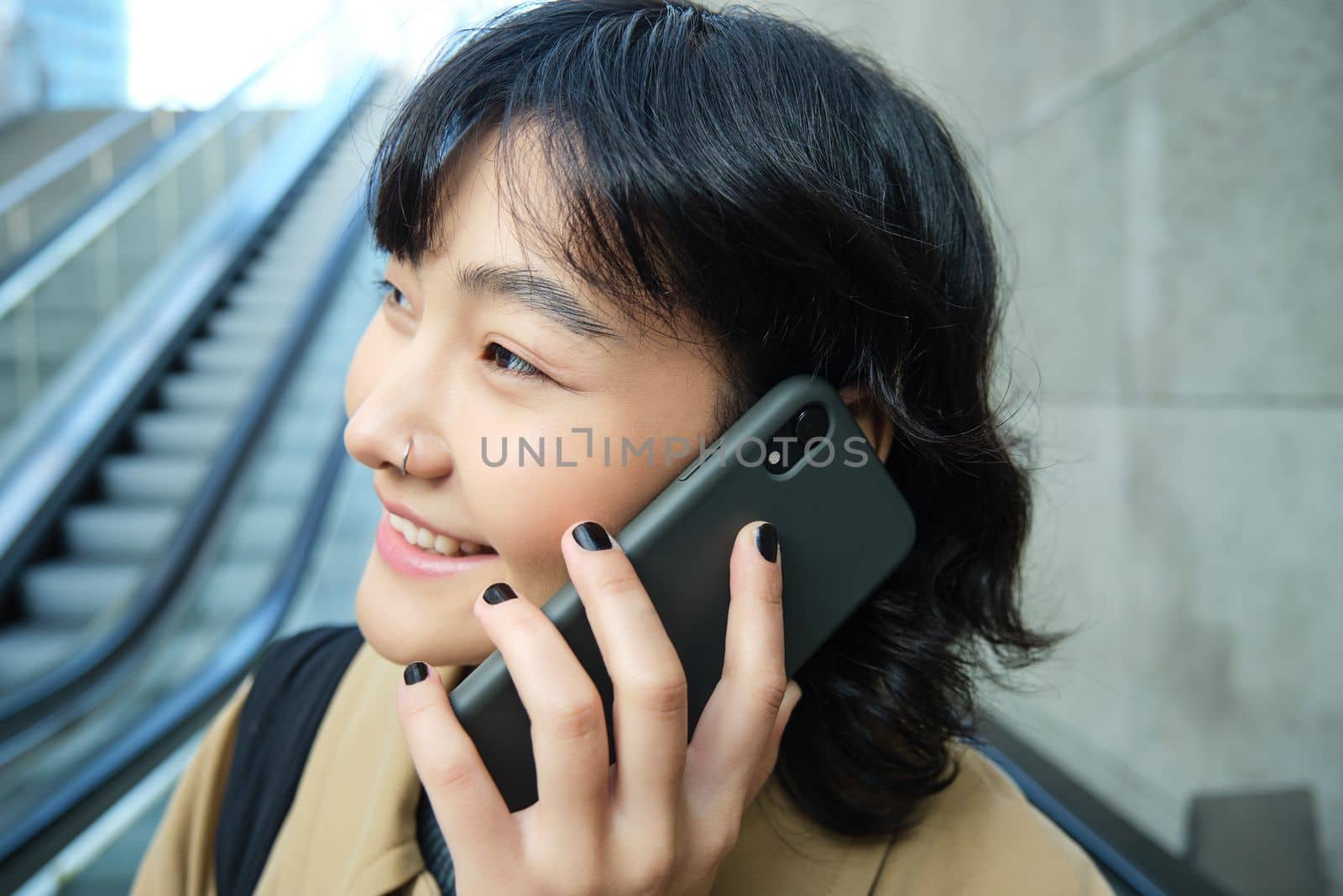 Headshot of smiling korean woman with smartphone, makes a phone call, goes down escalator in city, commutes to university.