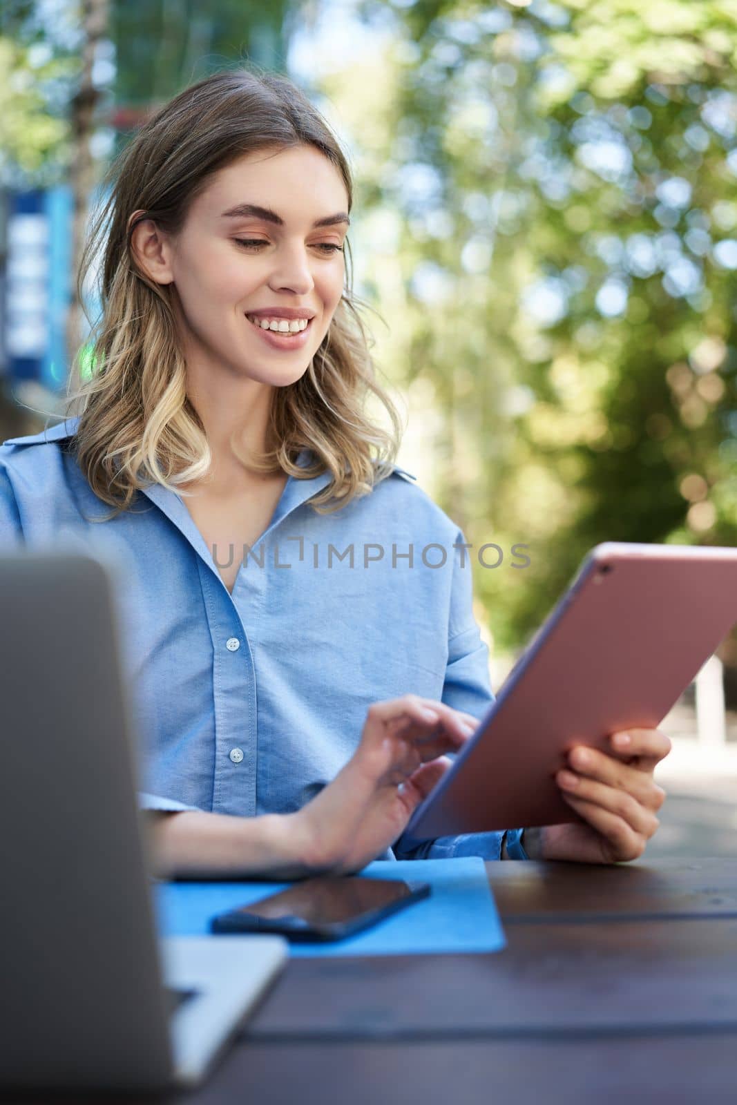 Vetical shot of young female student, reading on digital tablet, studying outdoors. Businesswoman sitting outside with laptop and gadgets, working.