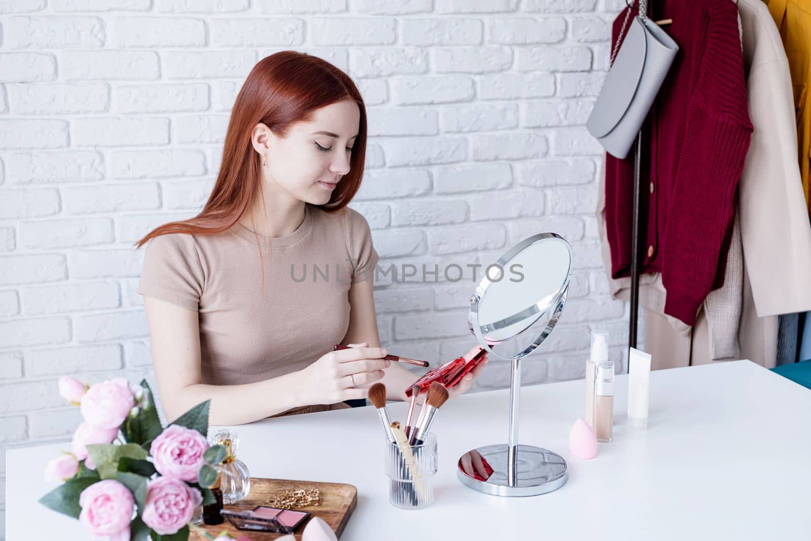 young beautiful woman holding make-up brushes and making up with cosmetics set at home