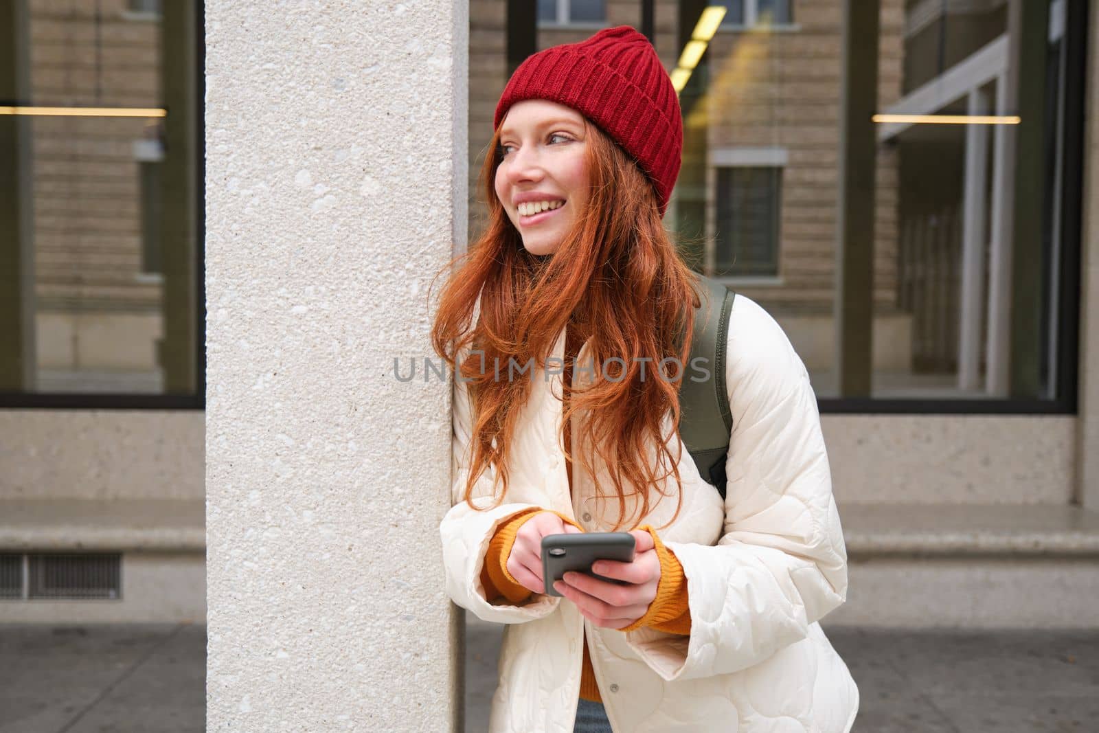 Beautiful redhead girl with smartphone, standing on street, holding mobile phone, using taxi app, connects to public wifi and uses internet, sends a text message by Benzoix