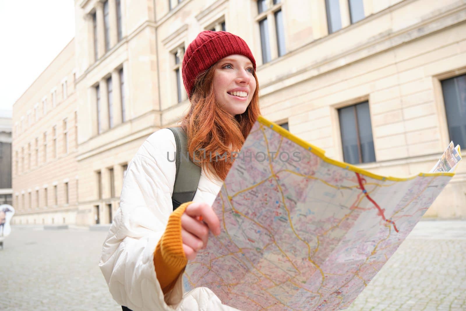 Beautiful redhead woman, tourist with city map, explores sightseeing historical landmark, walking around old town, smiling happily by Benzoix