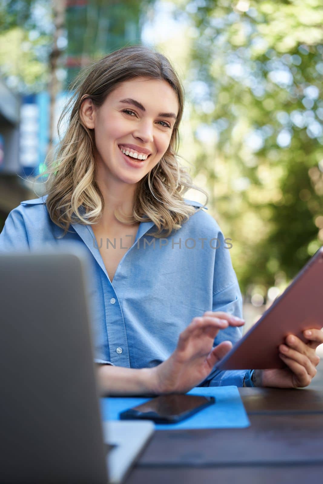 Vertical shot of smiling successful businesswoman, using digital tablet, sitting outdoors in park, working with laptop. Coporate people concept.