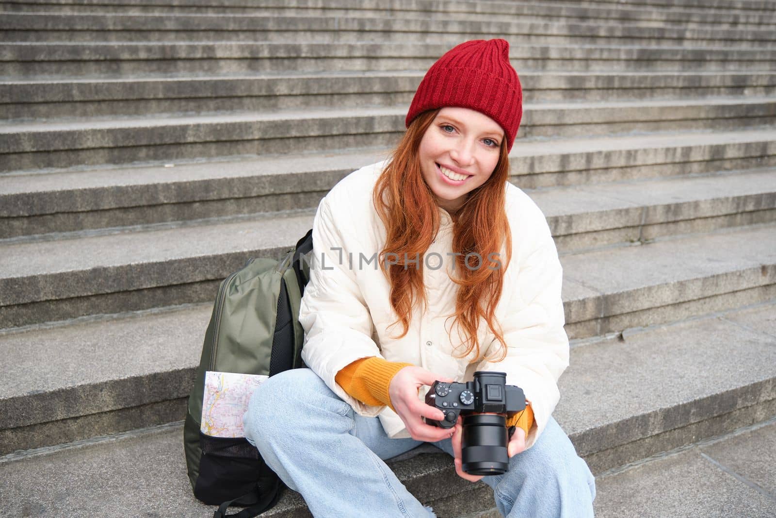 Portrait of young photographer girl, sits on stairs with professional camera, takes photos outdoors, making lifestyle shooting by Benzoix