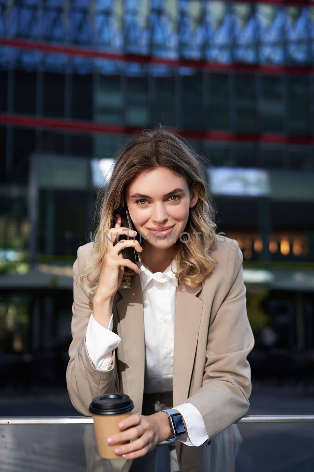 Vertical shot of smiling businesswoman answer mobile phone call, talking on smartphone and drinking coffee by Benzoix