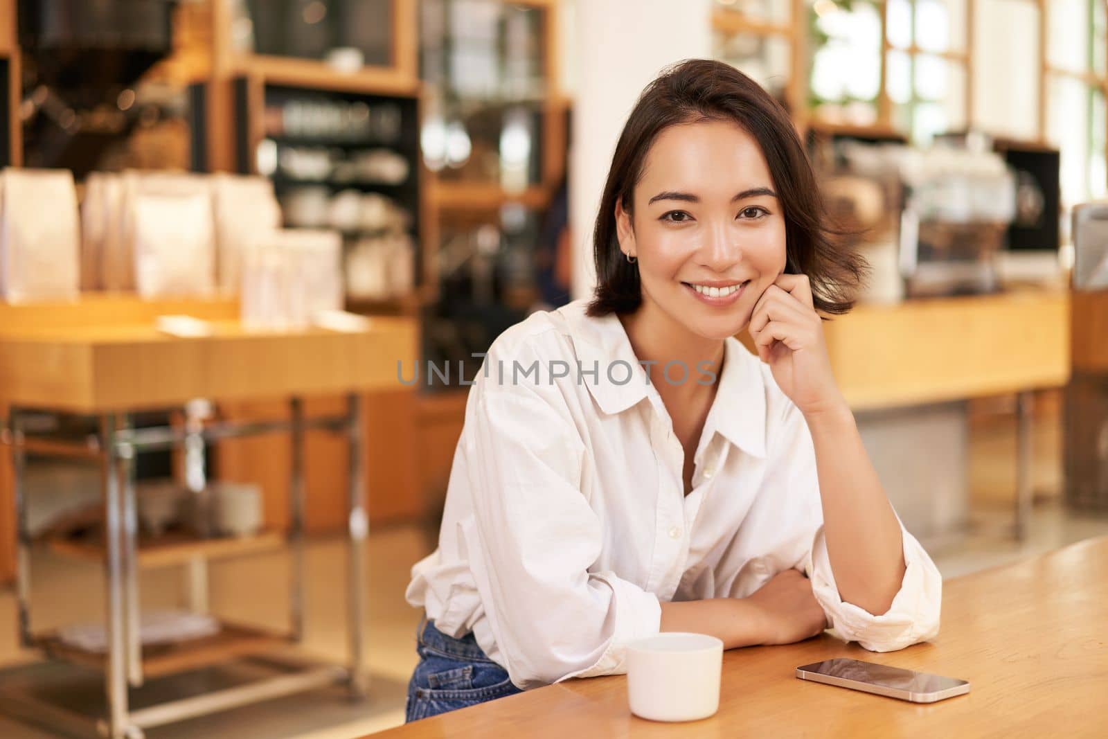 Portrait of confident asian woman, sitting in cafe, smartphone and coffee on table. Businesswoman smiling with confidence. Copy space