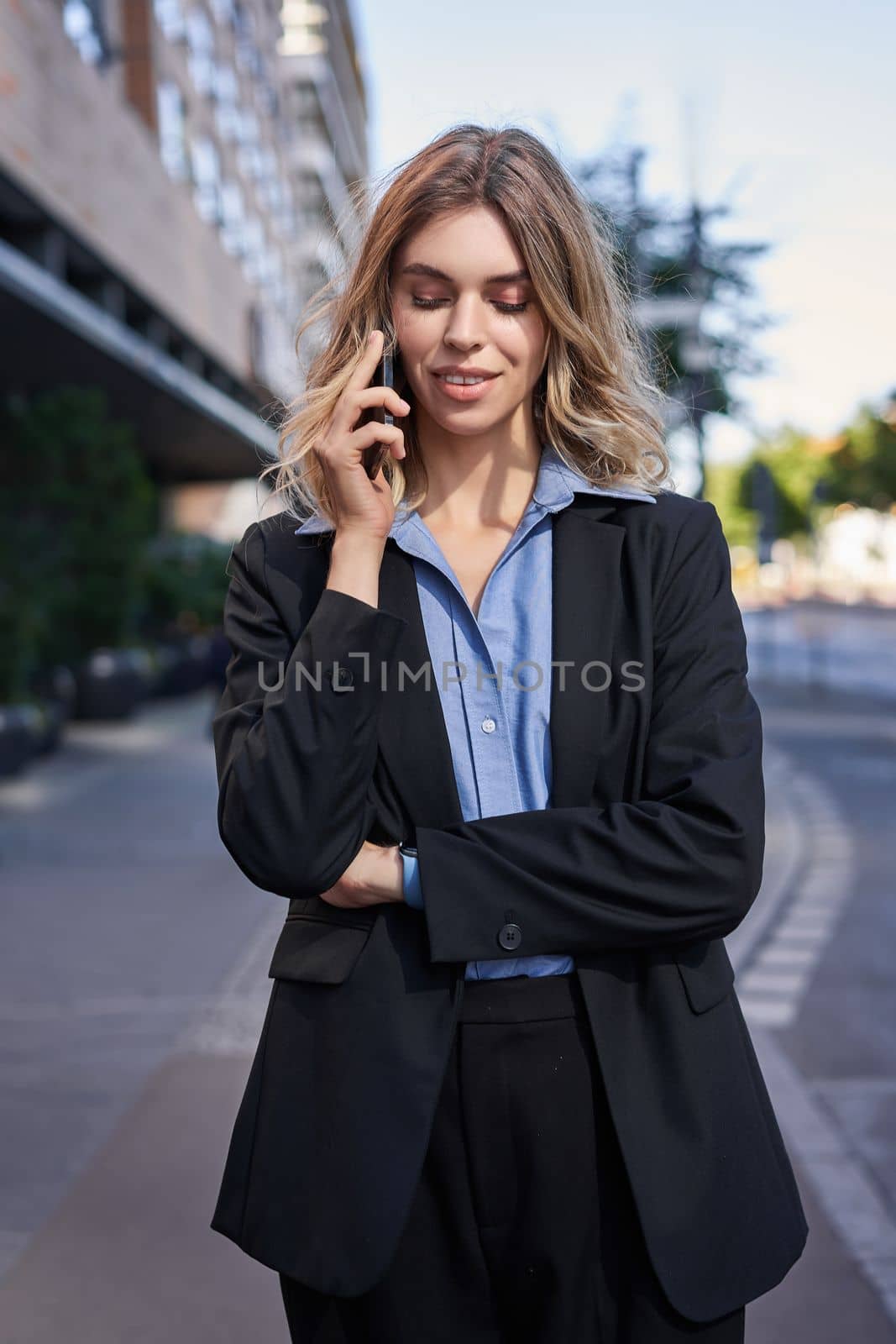 Vertical shot of confident young businesswoman making phone call, standing on street and talking on telephone by Benzoix