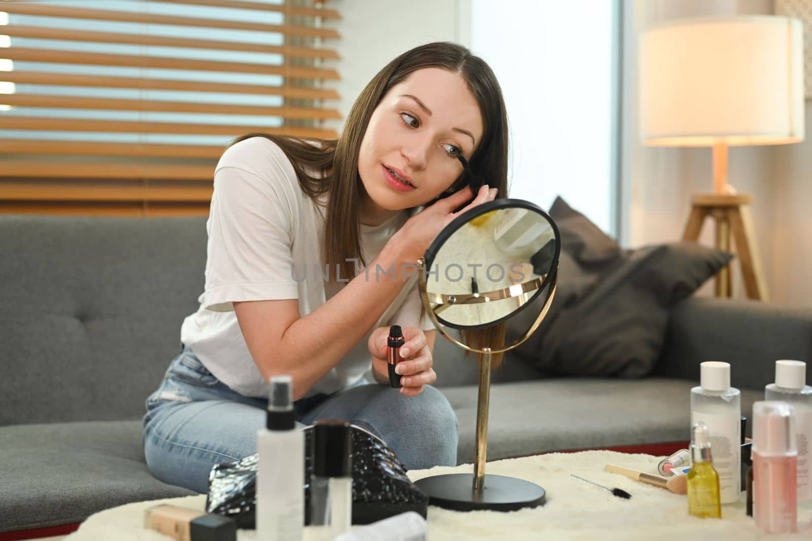 Beautiful caucasian woman applying mascara on eyelashes and looking into the mirror. Beauty and cosmetics concept.