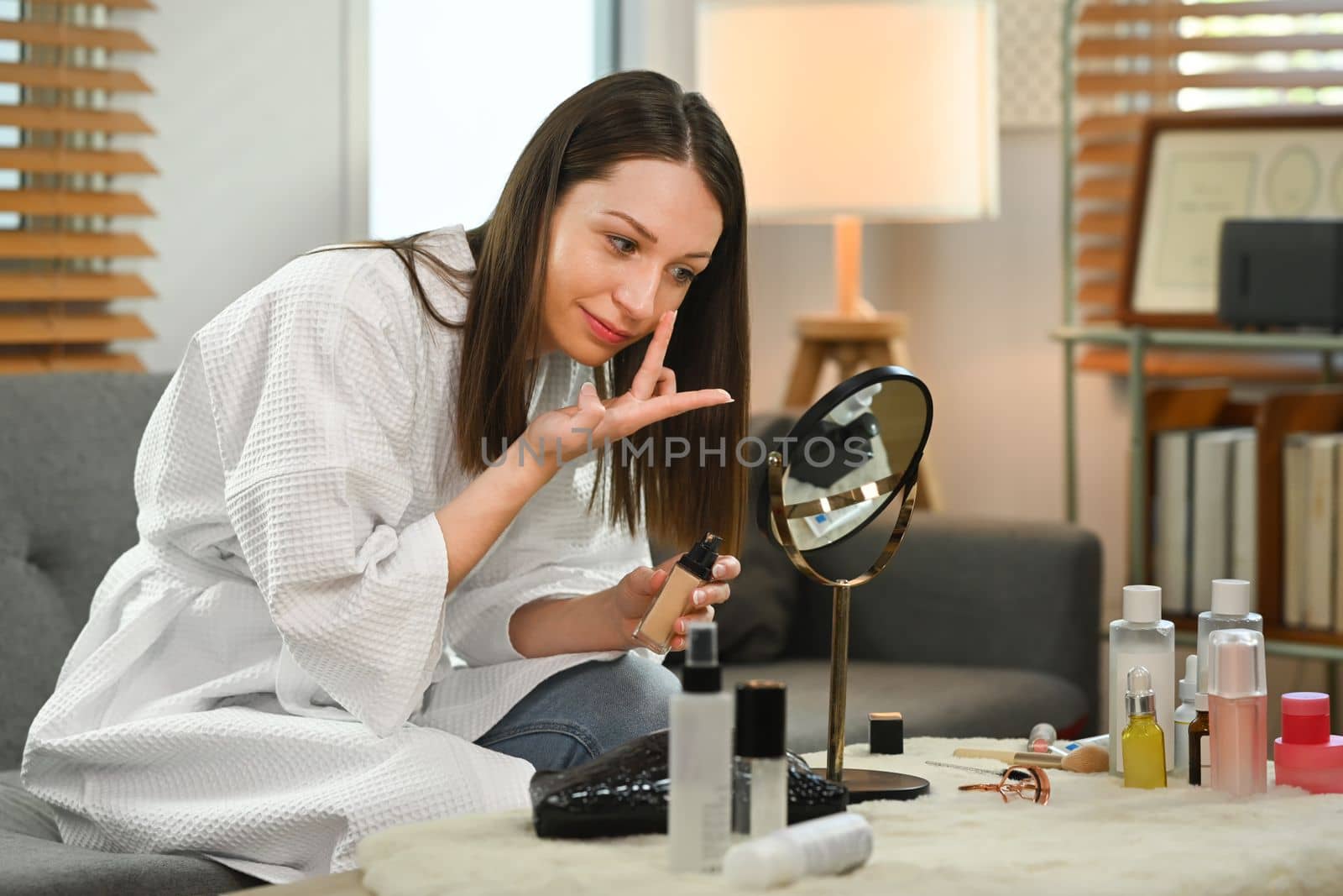 Attractive caucasian woman looking into the mirror and applying foundation on her face. Beauty and cosmetics concept.