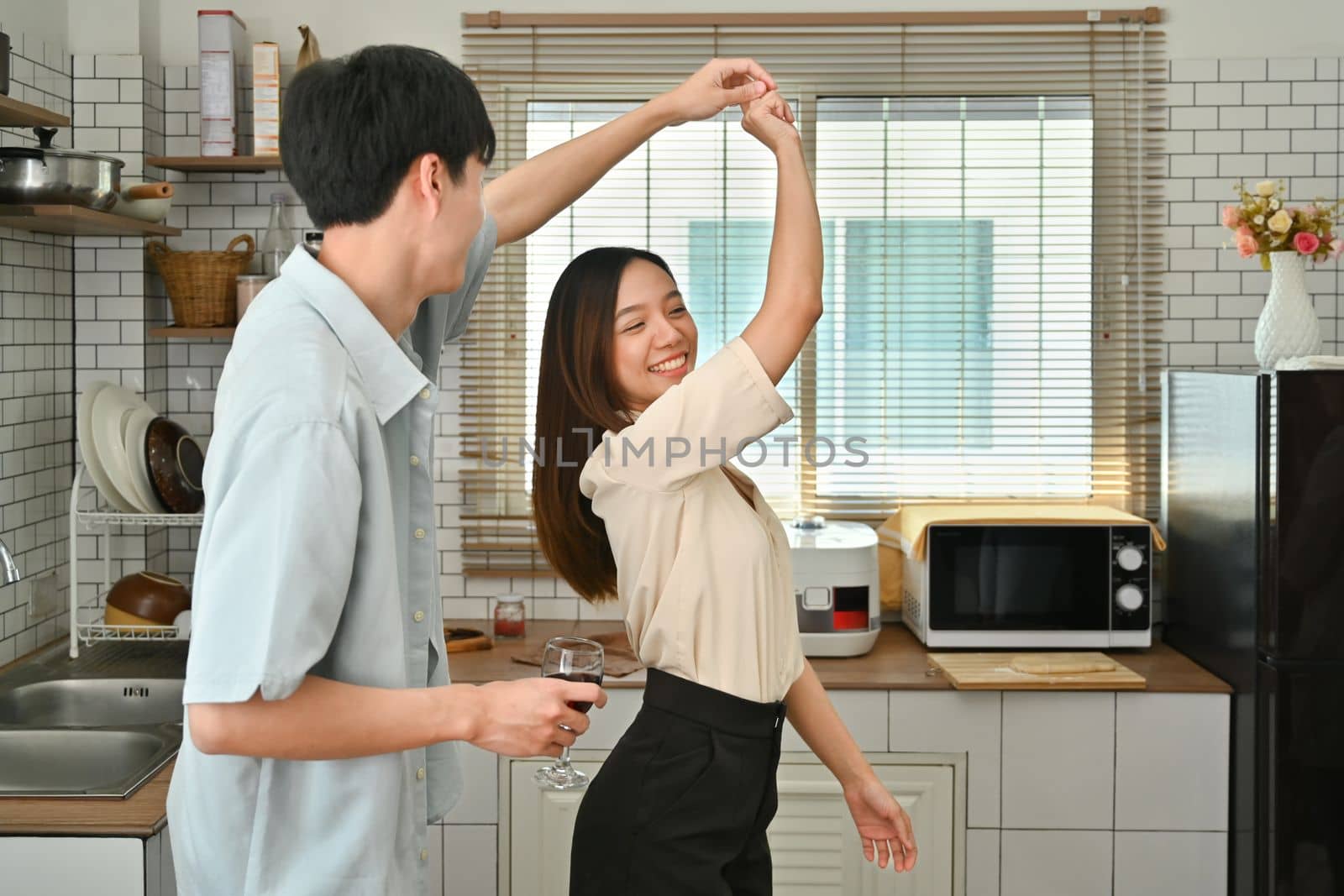 Cheerful young husband and wife dancing and have fun together in kitchen, spending leisure weekend time together at home by prathanchorruangsak