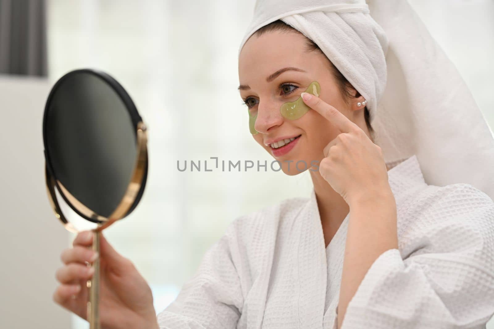 Gorgeous millennial caucasian woman in bathrobe using under eye patches. Self care and daily beauty routine.