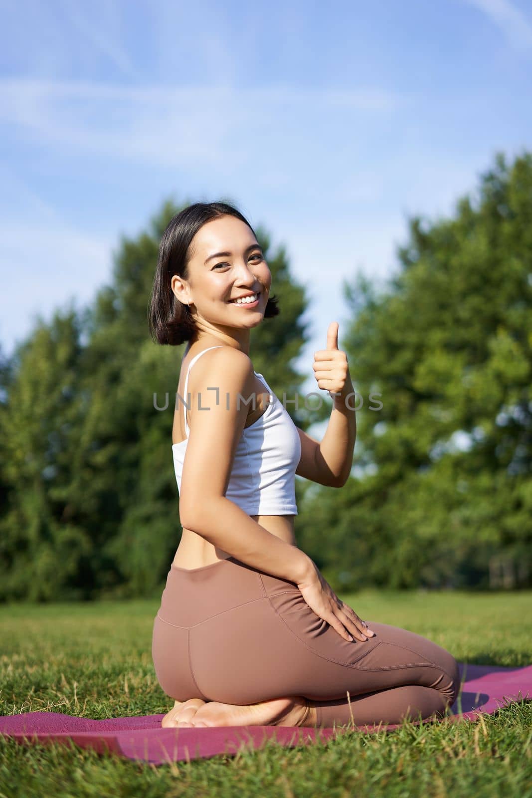 Portrait of asian woman say yes to yoga training in park, makes thumb up, sitting and meditating by Benzoix