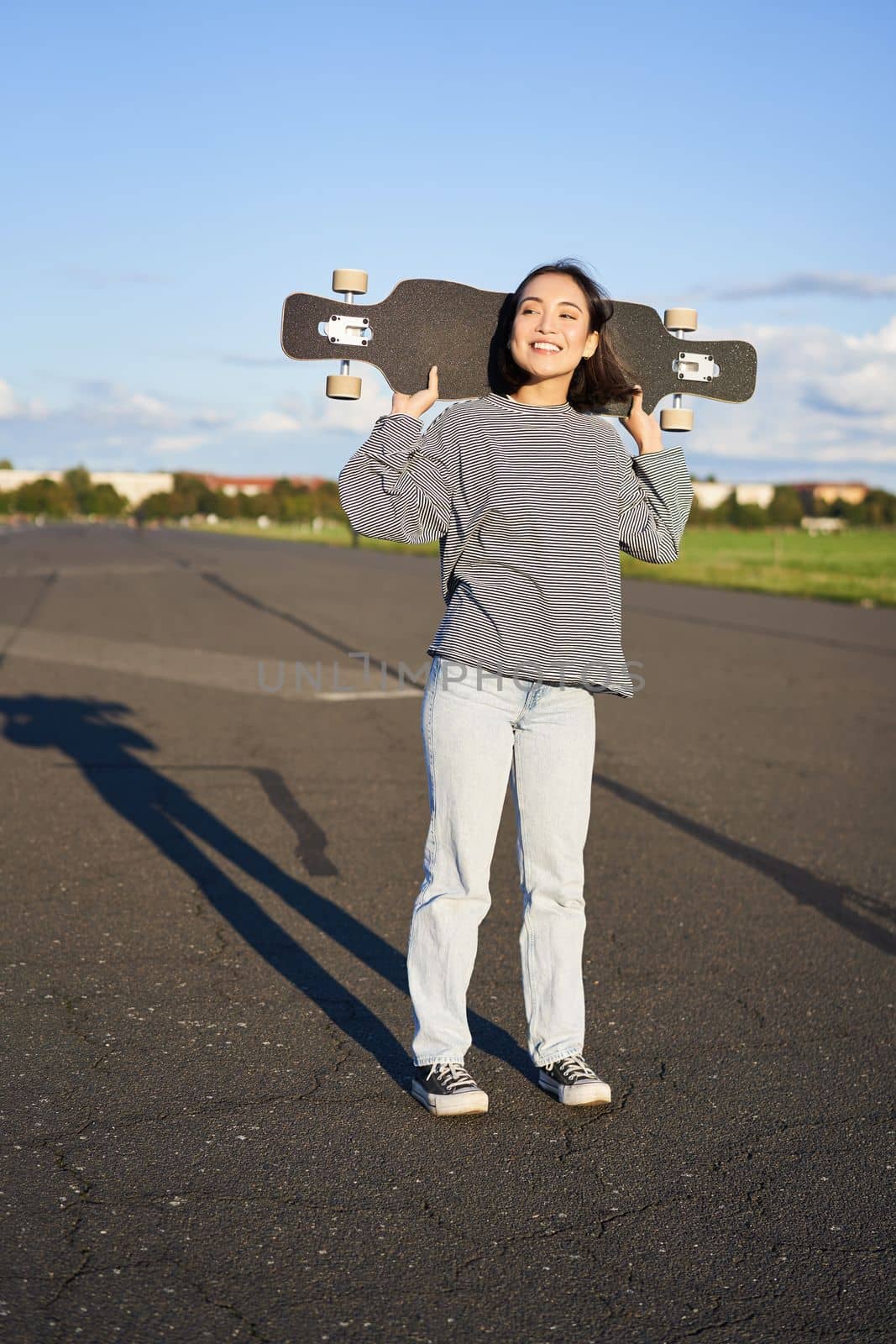 Lifestyle and people. Young asian girl posing with longboard, skating on her cruiser. Smiling woman holding skateboard on shoulders.