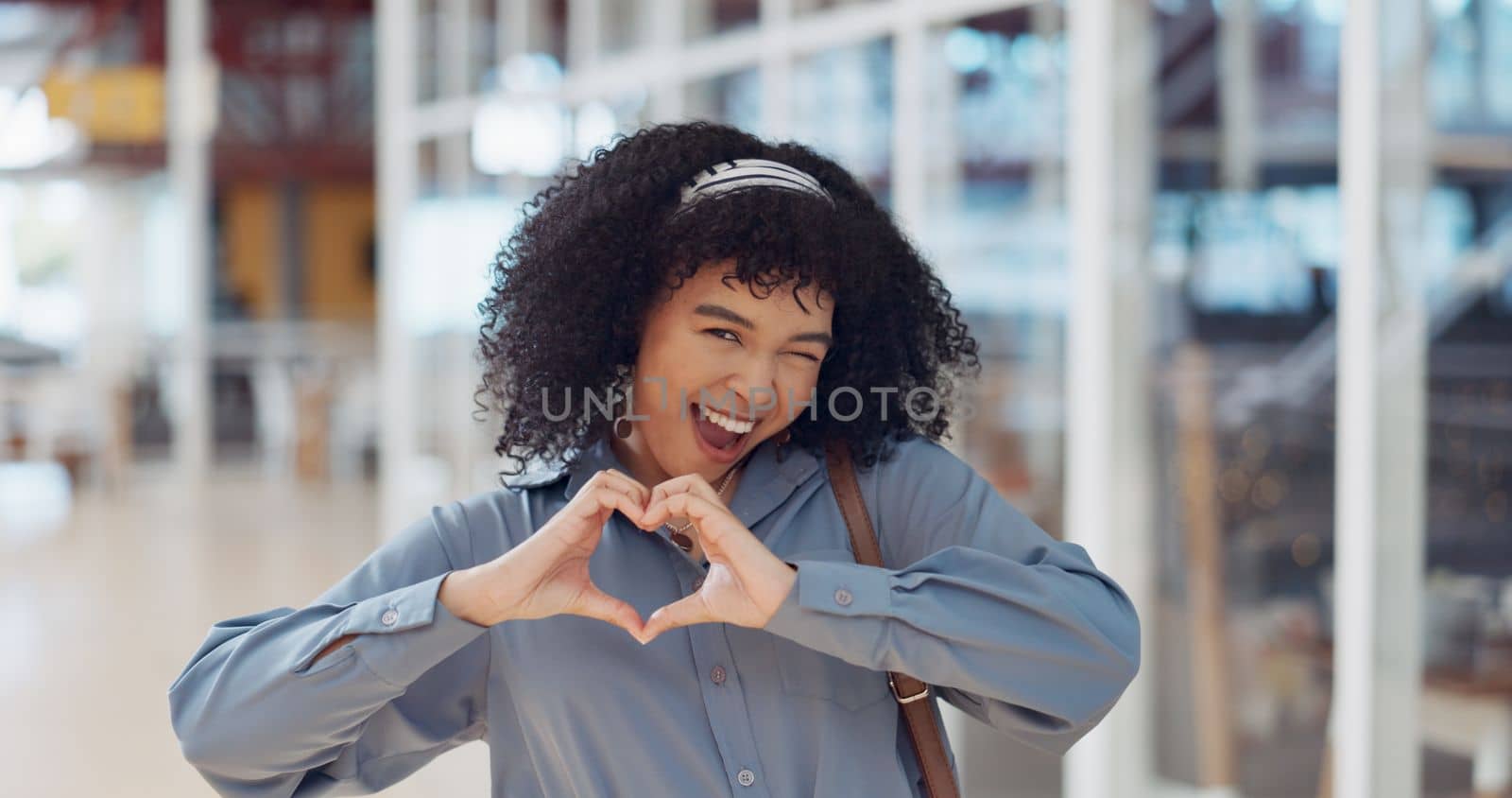 Hands, heart and love with a business black woman making a hand gesture alone in her office at work. Happy, smile and positive with a female employee gesturing a hand sign for romance or affection by YuriArcurs