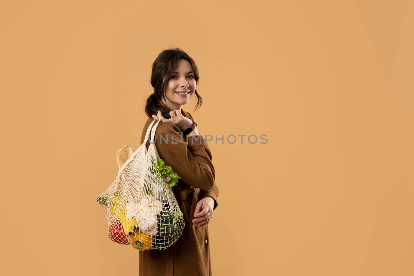 Young brunette woman holding reusable cotton shopping mesh bag with organic groceries from a market. Concept of no plastic. Zero waste, plastic free. Sustainable lifestyle