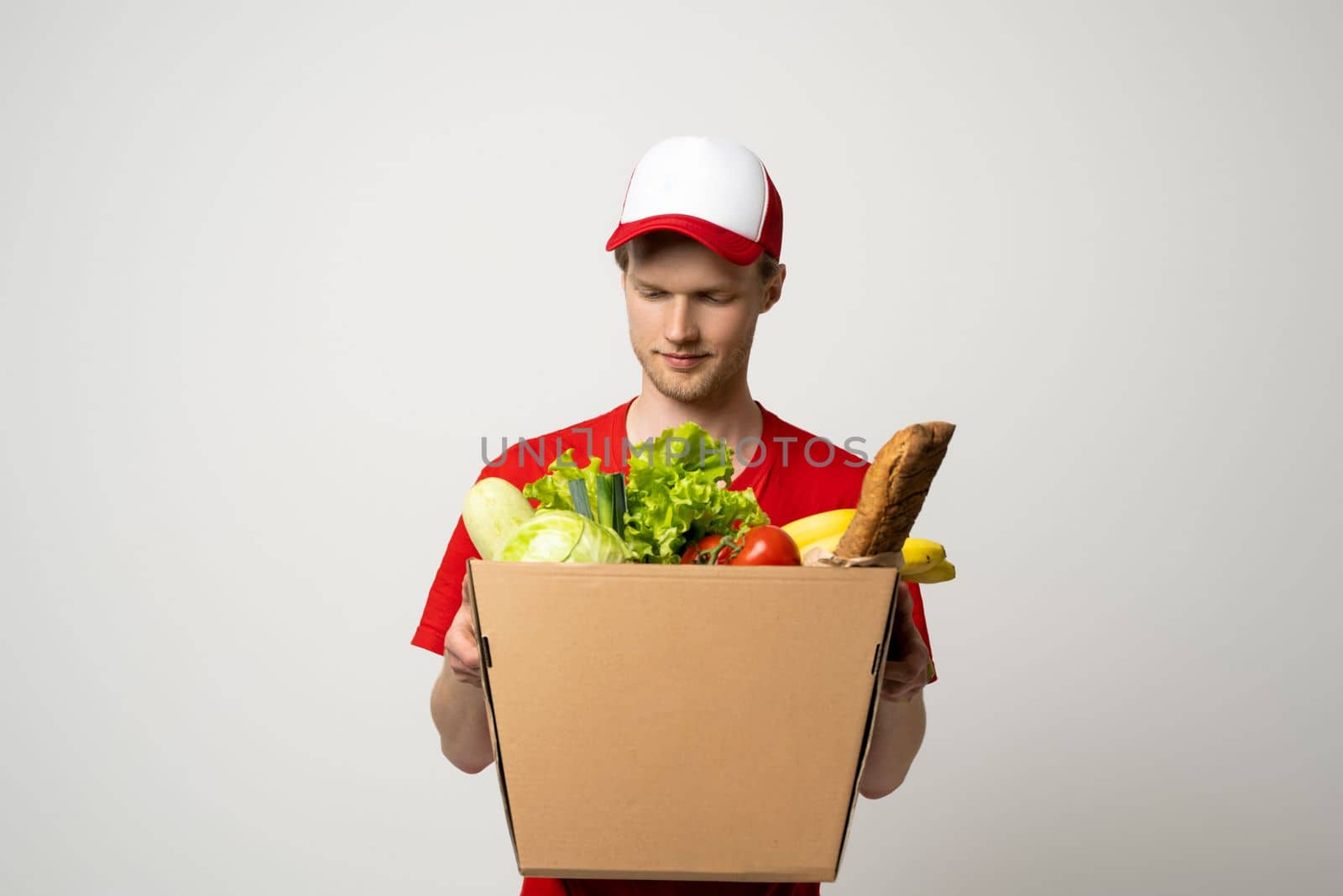 Handsome young delivery man carrying package box of grocery food, fruits, bread and drink from store. Delivery concept