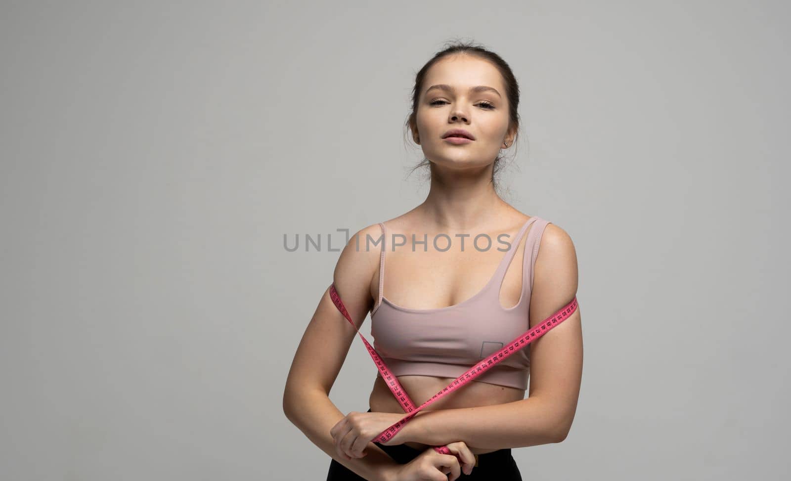 Brunette woman in sport outfit sportswear holding a pink measuring tape. Weight loss and diet concepts. Health care and healthy nutrition. Perfect slim body