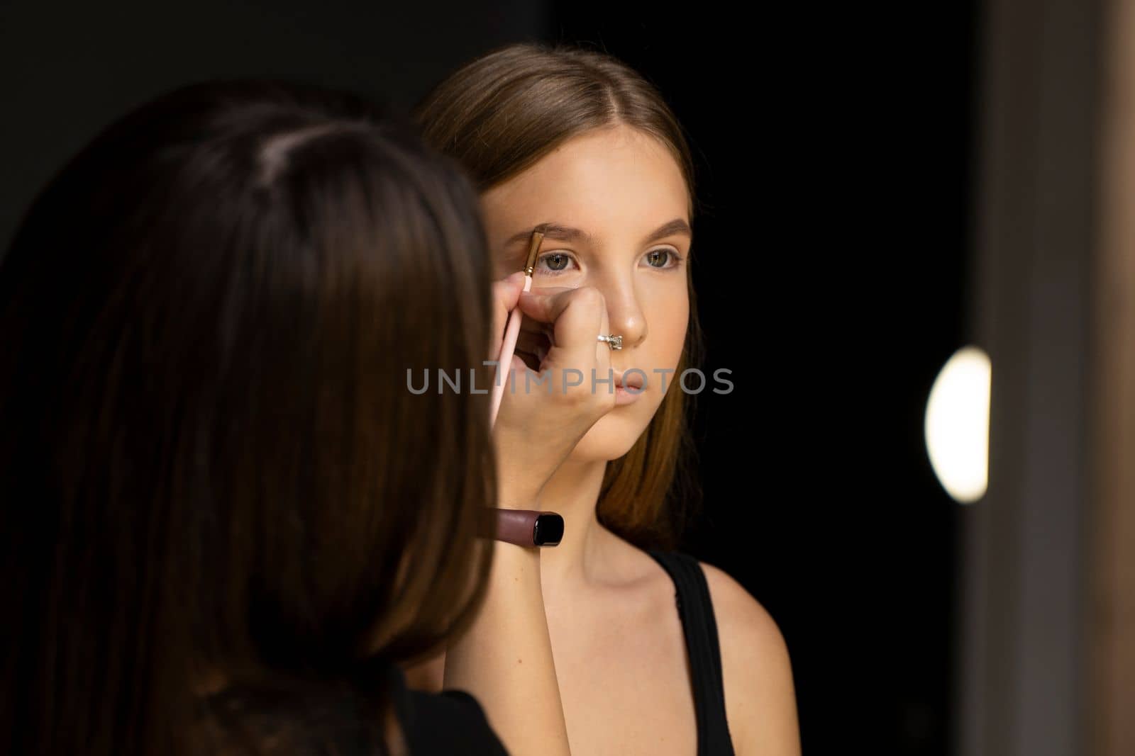 Close up makeup artist applies a make up on a model face. Beautiful woman with make-up face. Hand of visagiste, painting cosmetics of young beauty model girl