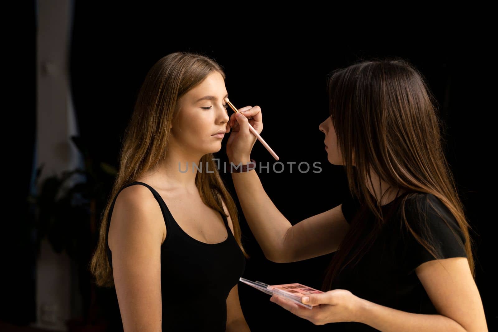 Hand of visagiste, painting cosmetics of young beauty model girl. Makeup artist applies a make up on a model face. Beautiful woman with make-up face. Make up in process