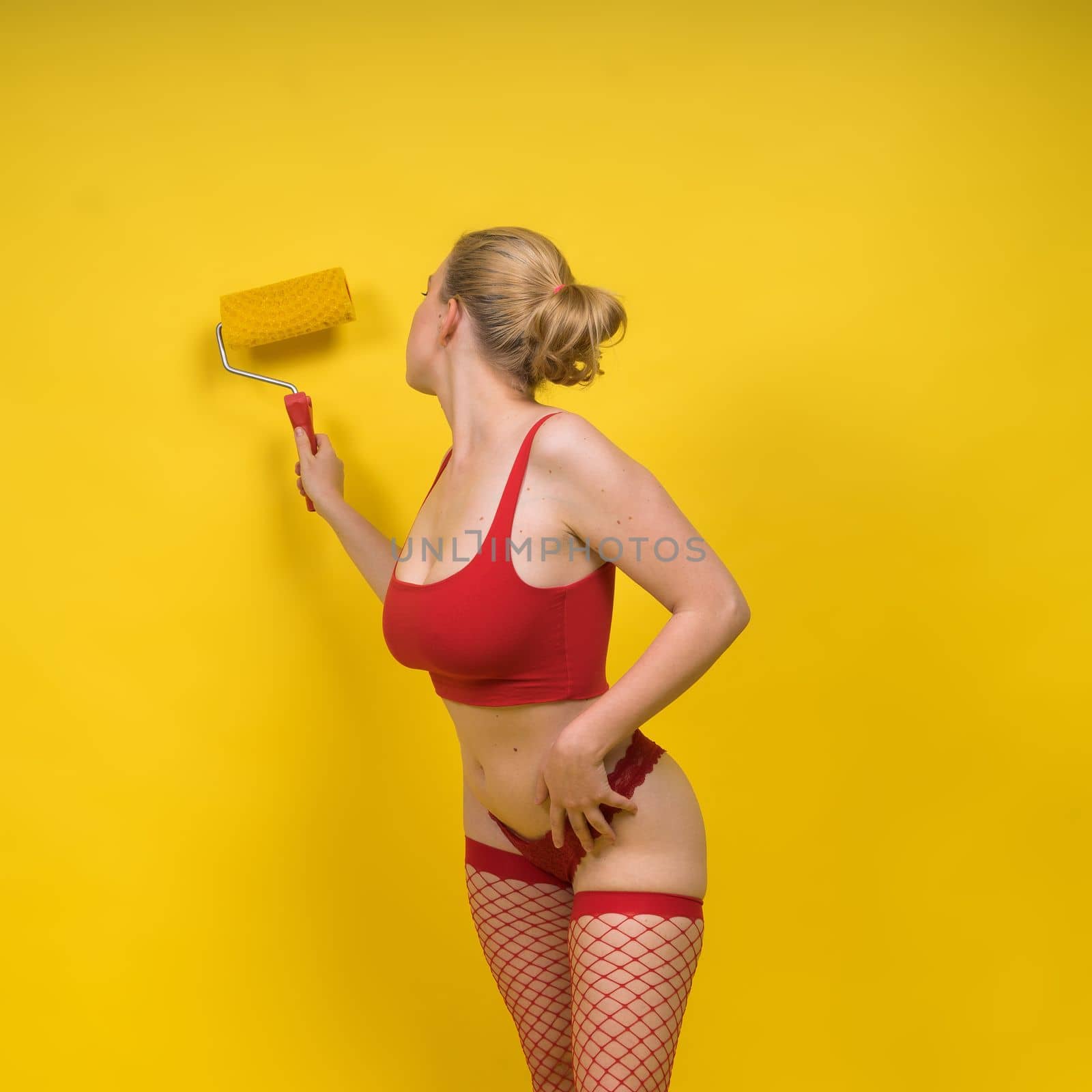 Beautiful blonde model wearing a short dress bodysuit is holding a roller brush. by Zelenin