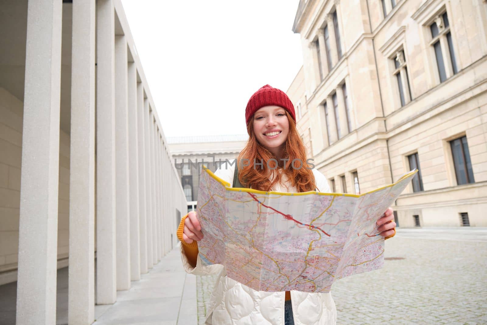 Beautiful redhead woman, tourist with city map, explores sightseeing historical landmark, walking around old town, smiling happily.