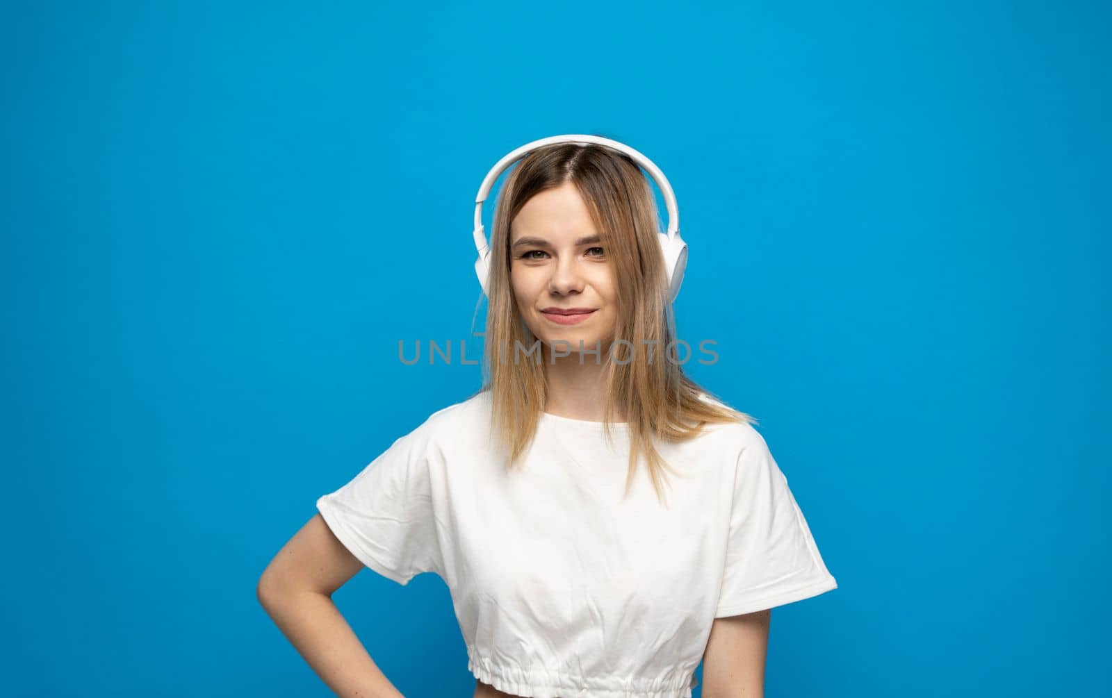 Beautiful bonde young woman in white headphones listening to music on blue background