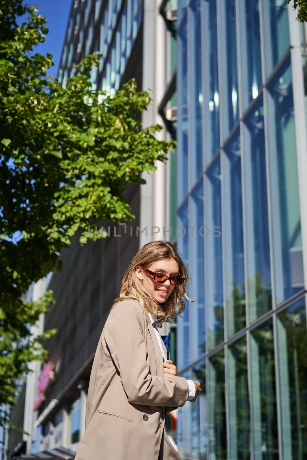 Portrait of confident saleswoman going to work, wearing sunglasses and suit. Businesswoman on her way to office, posing outdoors.