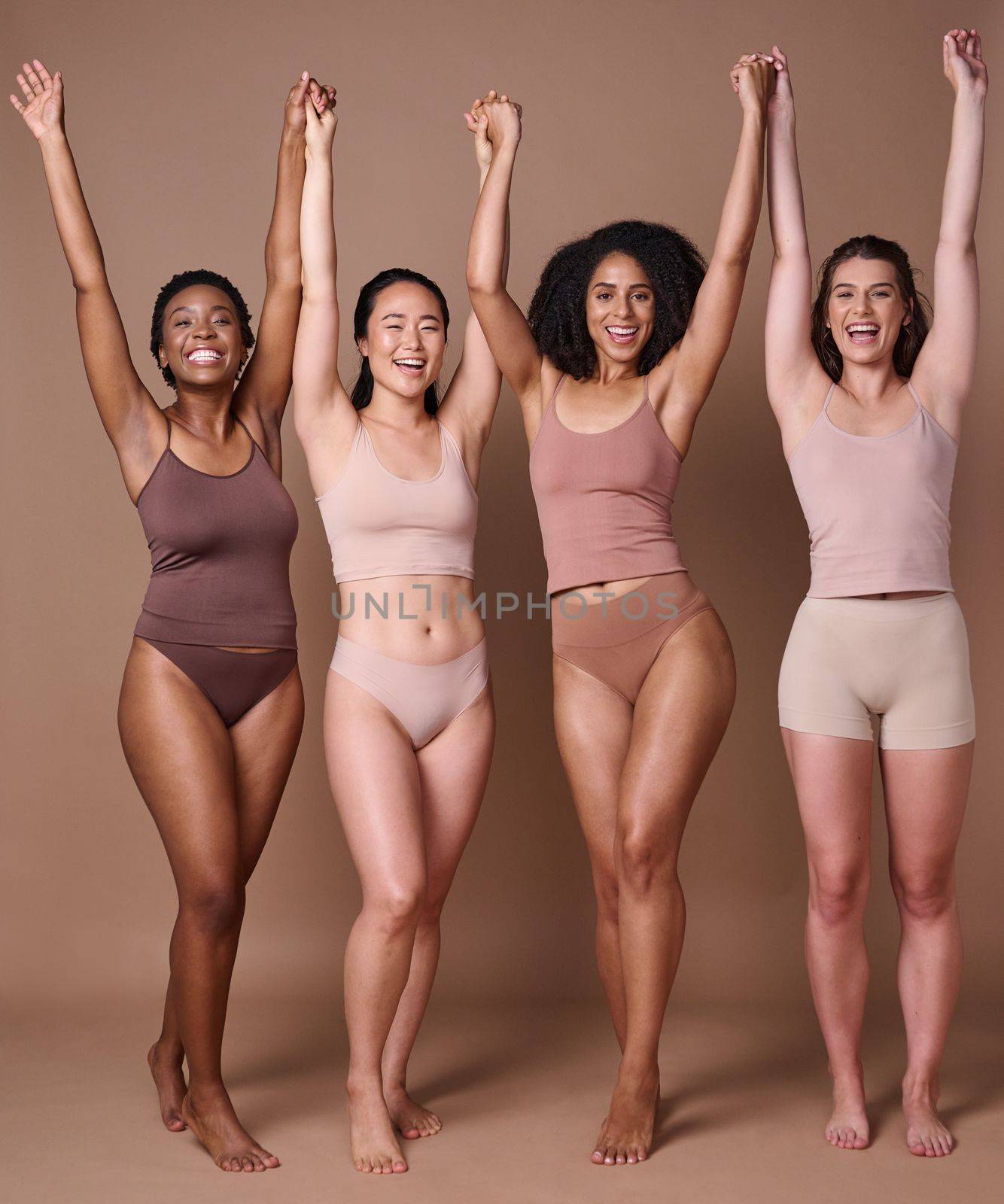 Diversity, women and natural beauty friends in studio in brown background with hands raised in celebration and support together. Diverse woman, underwear and celebrate body care or healthy lifestyle by YuriArcurs