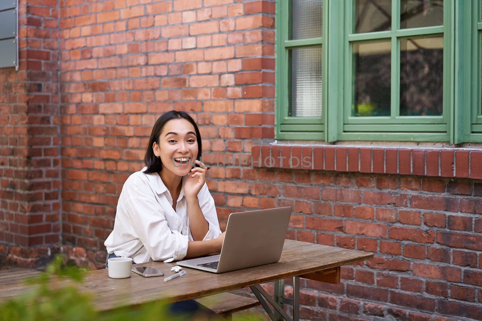 Enthusiastic asian woman sitting with laptop, laughing and smiling, looking happy, working remote online.