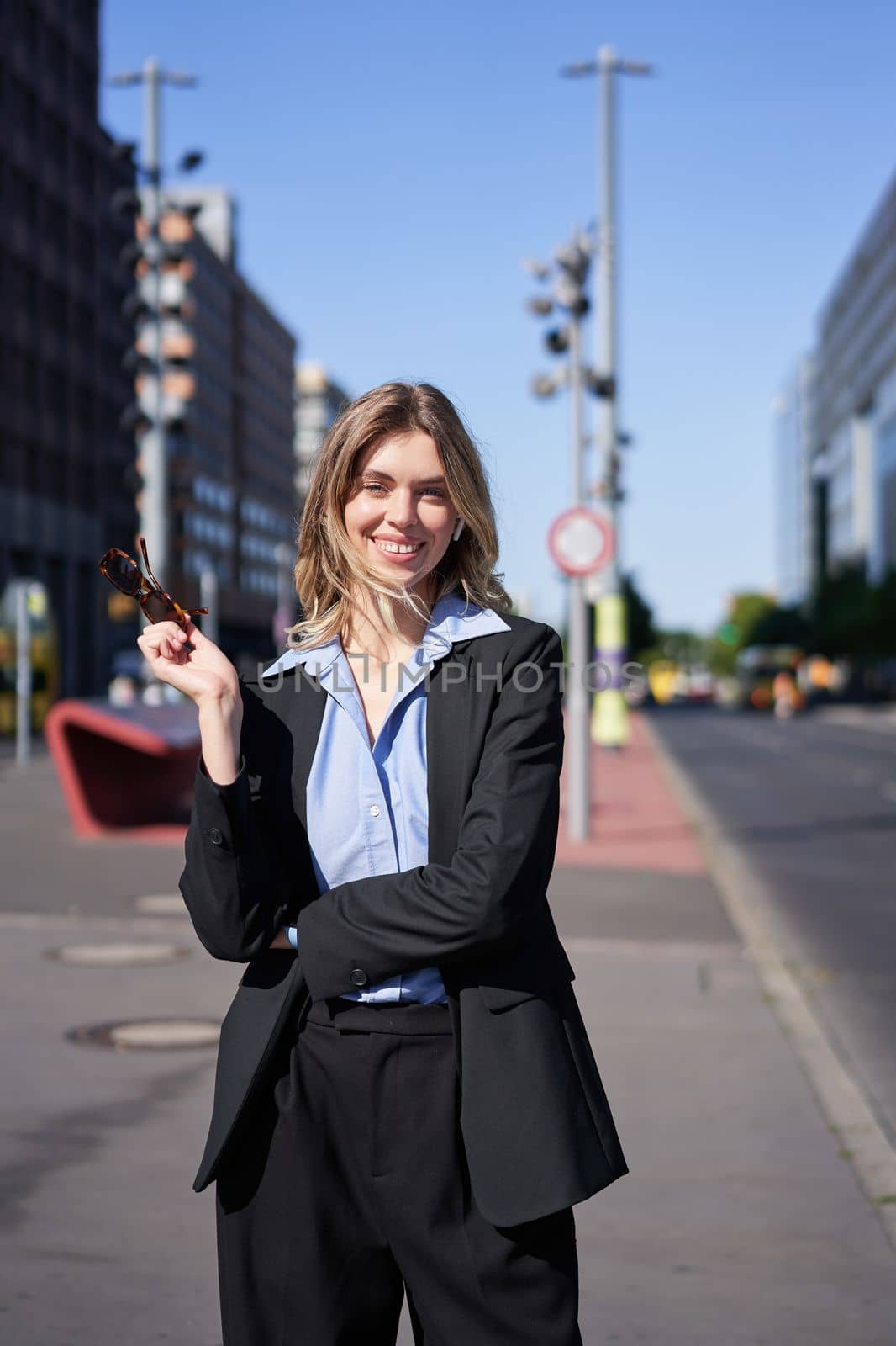 Portrait of successful young company ceo, businesswoman in black suit, standing on sunny street and smiling by Benzoix