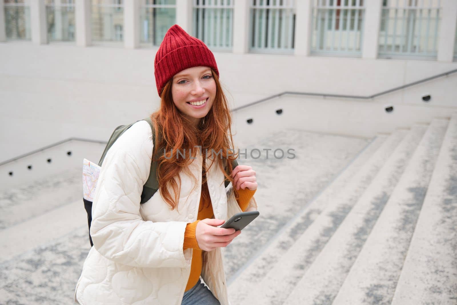 Smiling redhead girl, student tourist walks around city, goes up the stairs, looks at mobile phone map to get around town, sends message on smartphone.