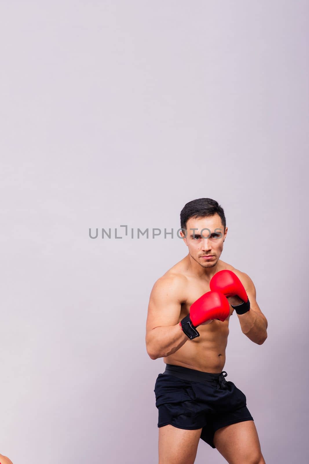 Muscular model sports young man in a boxing gloves on grey background. Male flexing his muscles.