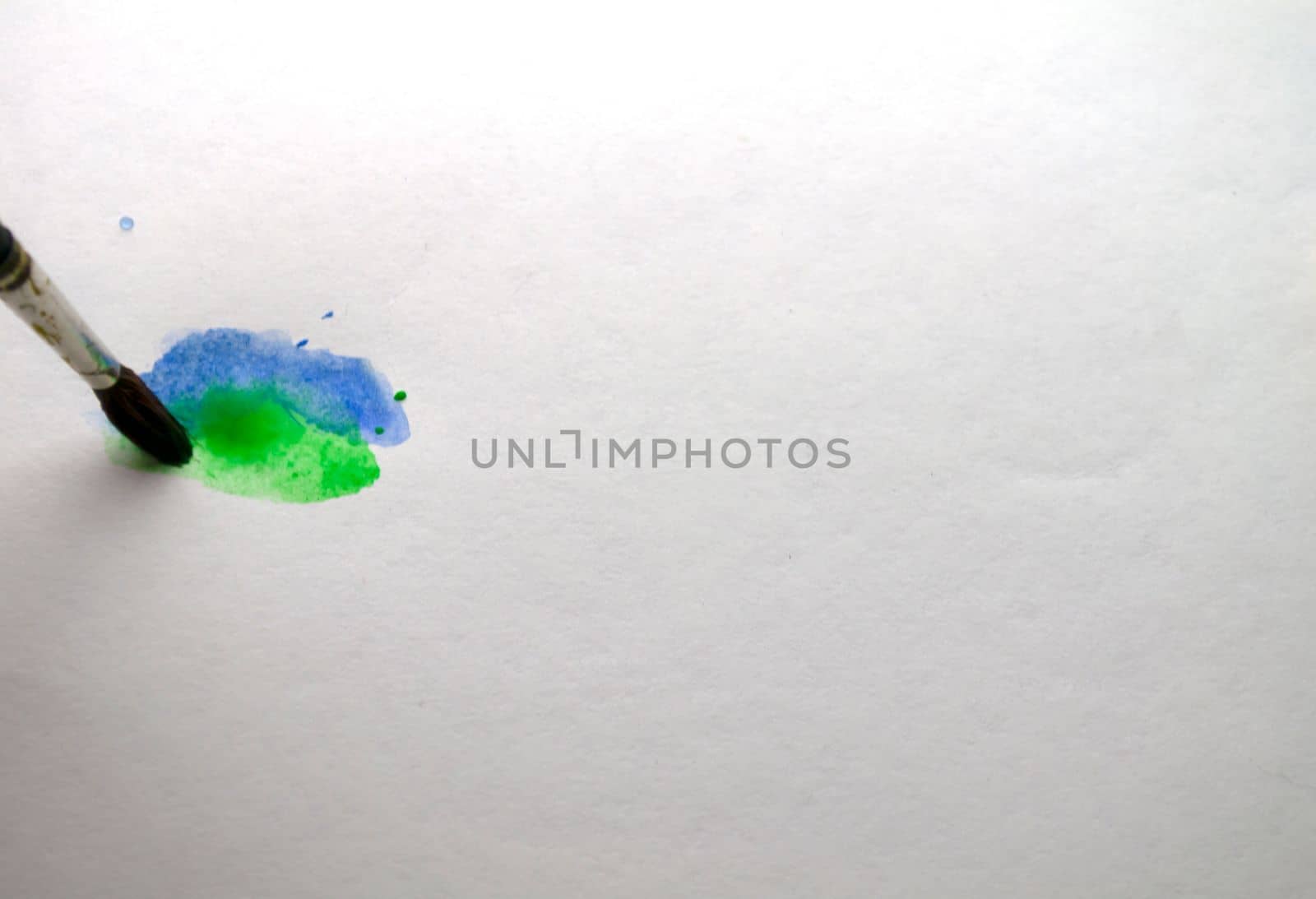 The brush draws blue and green paint. The brush draws on white paper with blue and green watercolor paint.