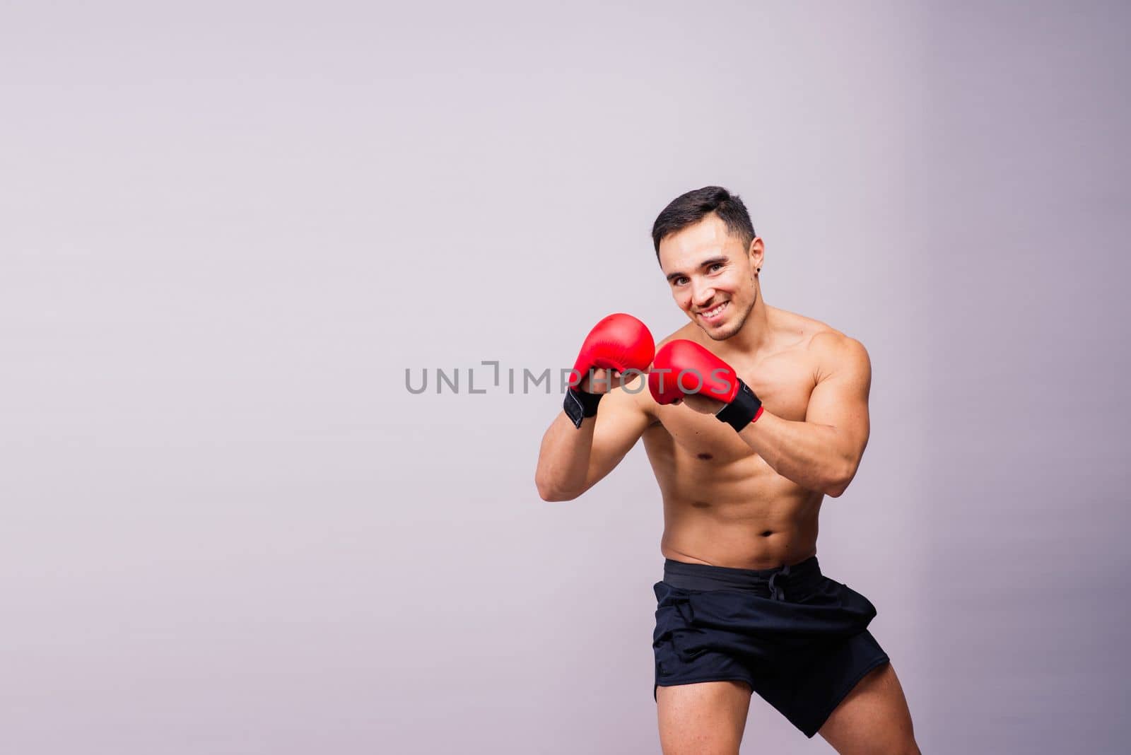 Muscular model sports young man in a boxing gloves on grey background. Male flexing his muscles.