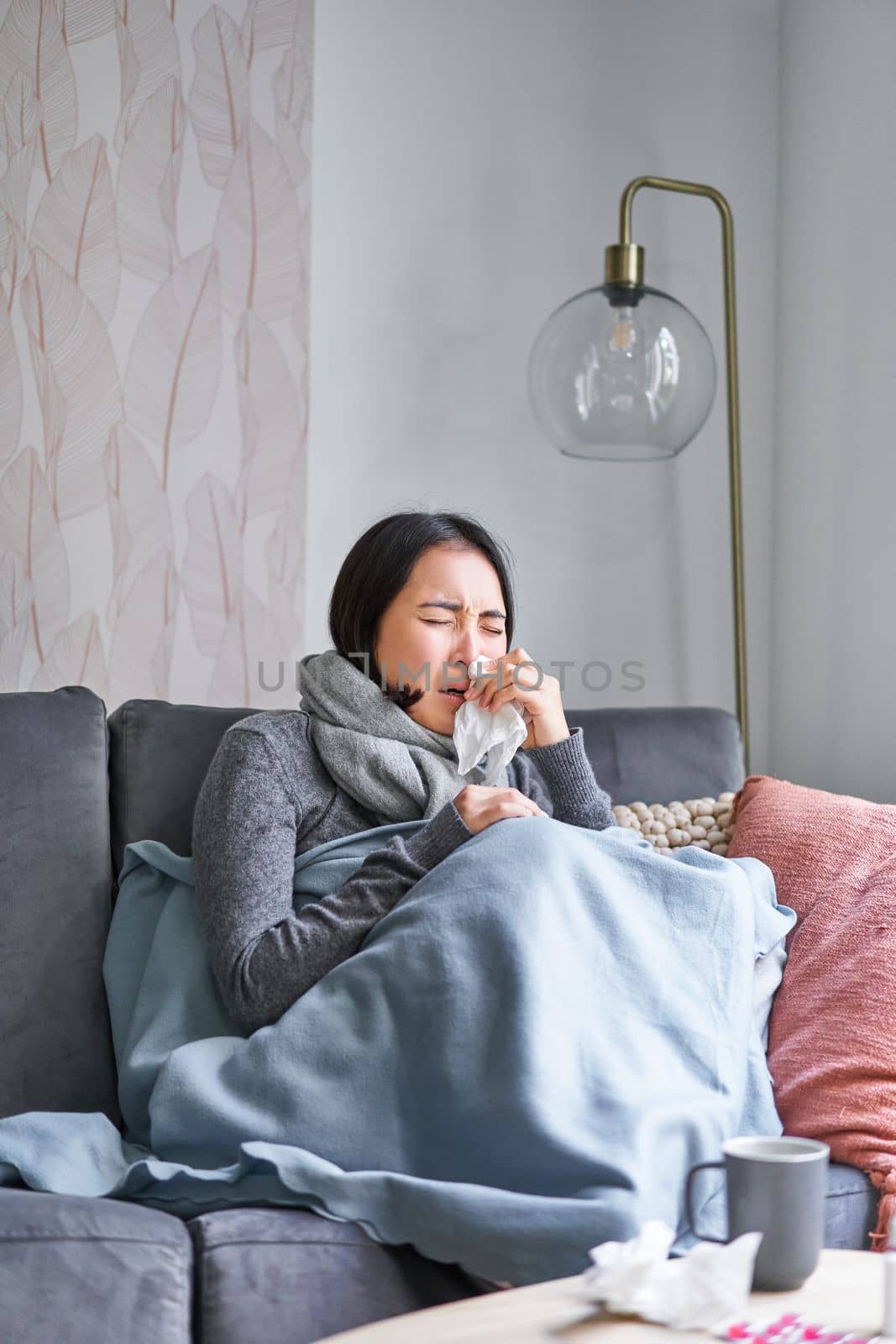 Korean woman feels unwell, sneezing and coughing, catching cold, staying at home with fever and temperature, taking medication.